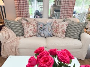 A white sofa with floral and plaid pillows shows how to refresh your home for summer with a striped blanket and pink roses.