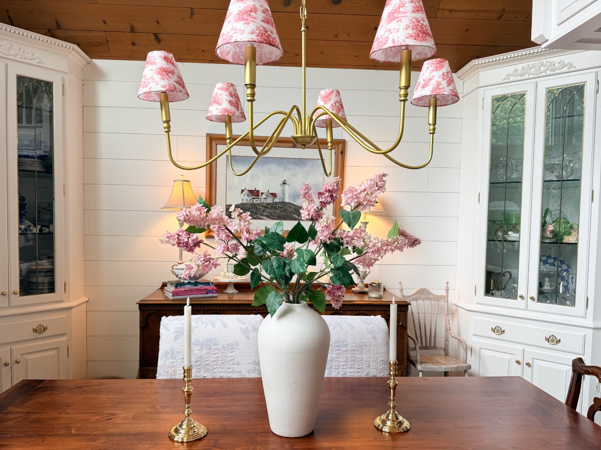 White vase with pink flowers, gold candlesticks, and a chandelier—a perfect way to refresh your home for summer.