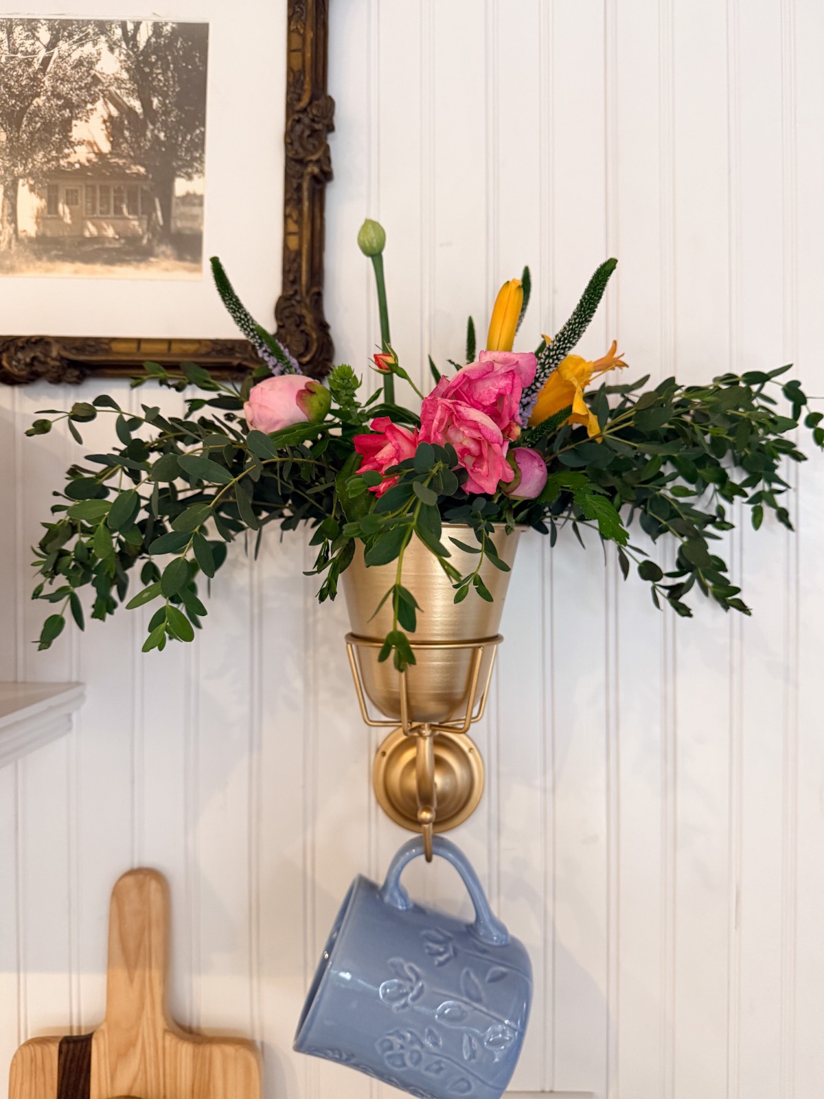 Gold wall vase with flowers, blue mug, and framed photo—an easy way how to refresh your home for summer.