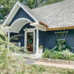 Blue house with a wooden door, white trim, and porch—discover how to decorate a small home beautifully with lush green plants.