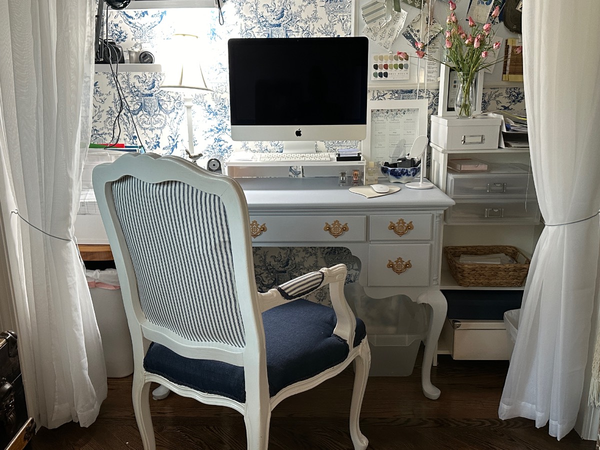 A vintage-style desk setup showing how to decorate a small home beautifully with organized supplies and elegant white curtains.
