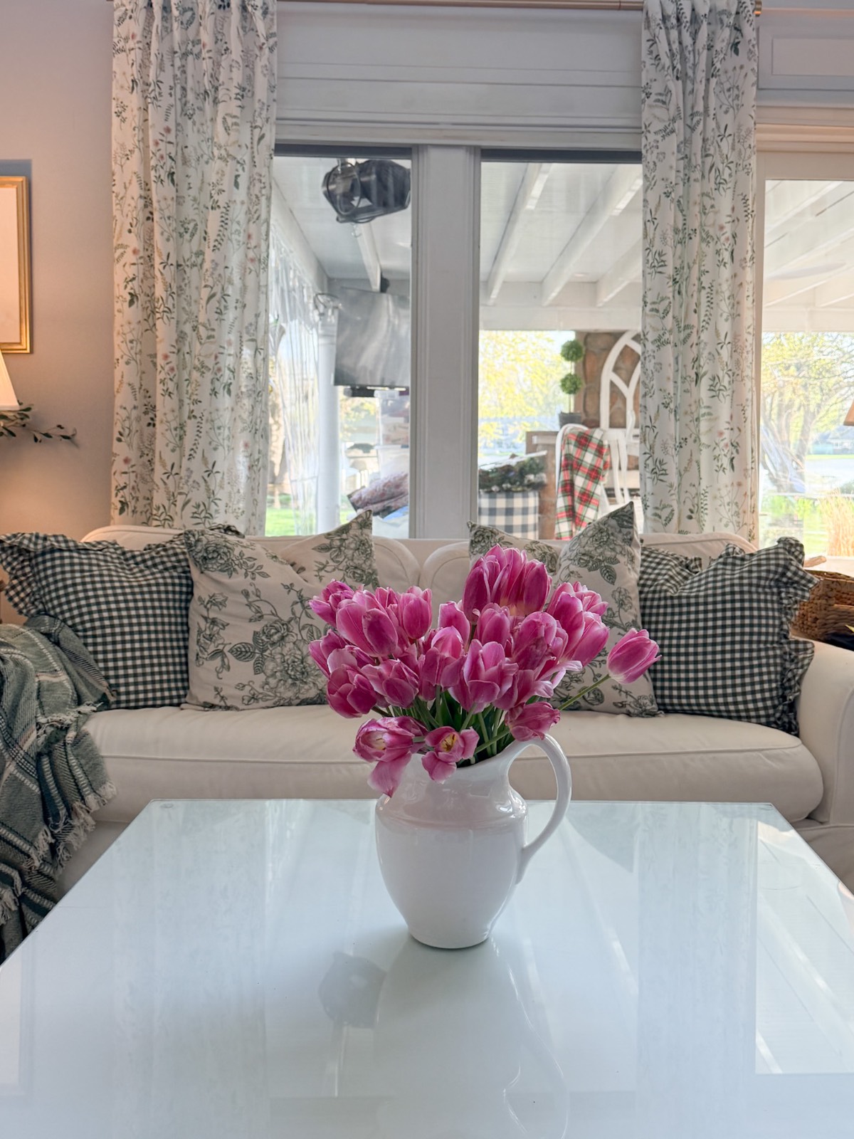 A white sofa with patterned pillows and pink tulips shows how to decorate a small home beautifully in a bright living room.