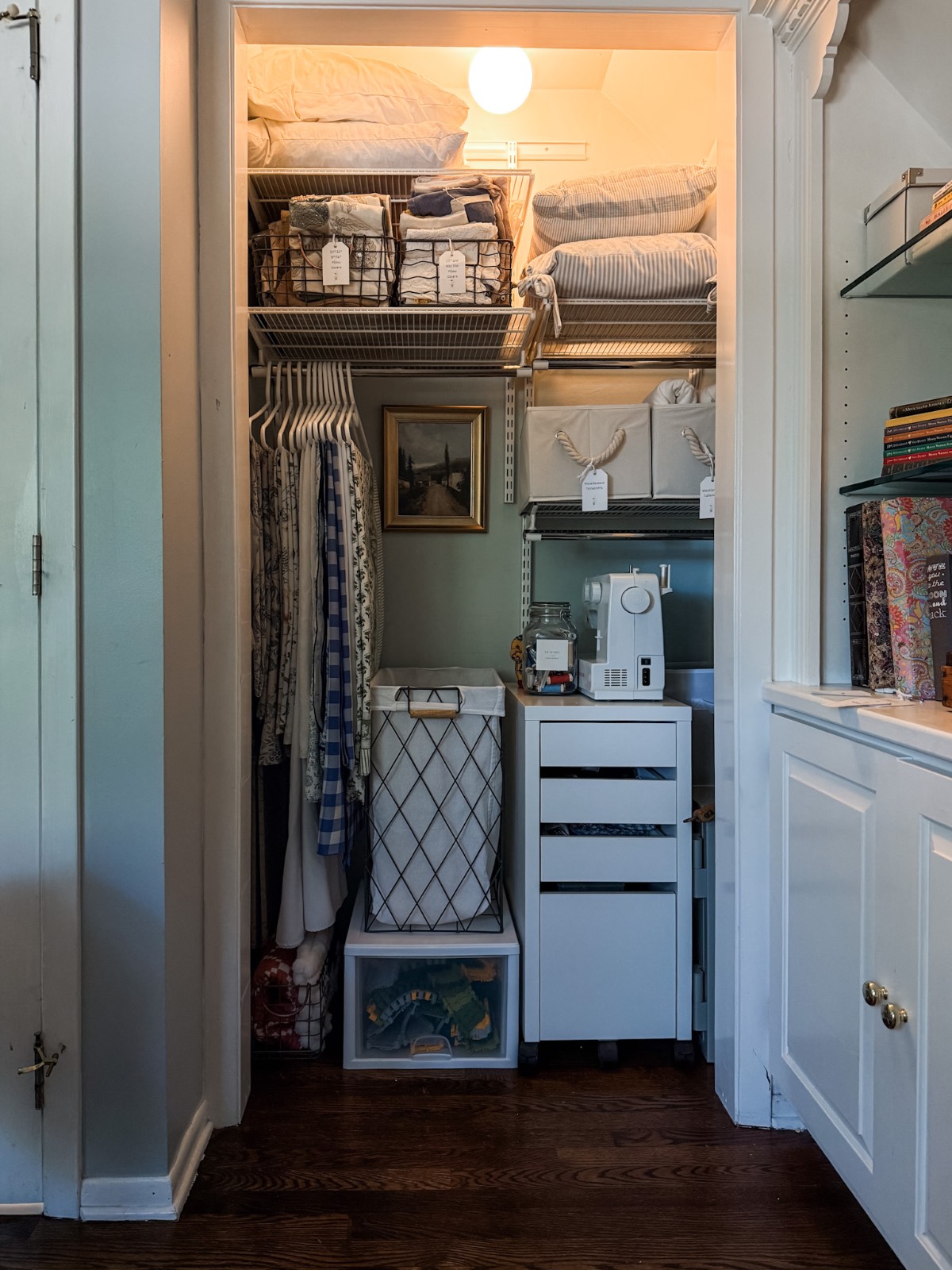 Closet transformation: organized clothes, linens, baskets, hamper, sewing machine, drawers, and art on the wall.
