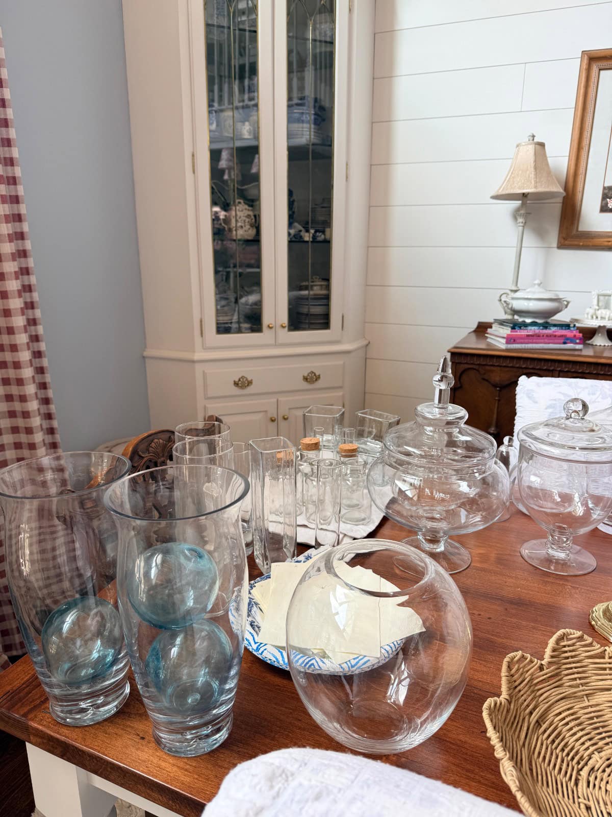 Glassware, jars, and plates arranged for a hosting closet transformation in a cozy room with white cabinet and lamp.