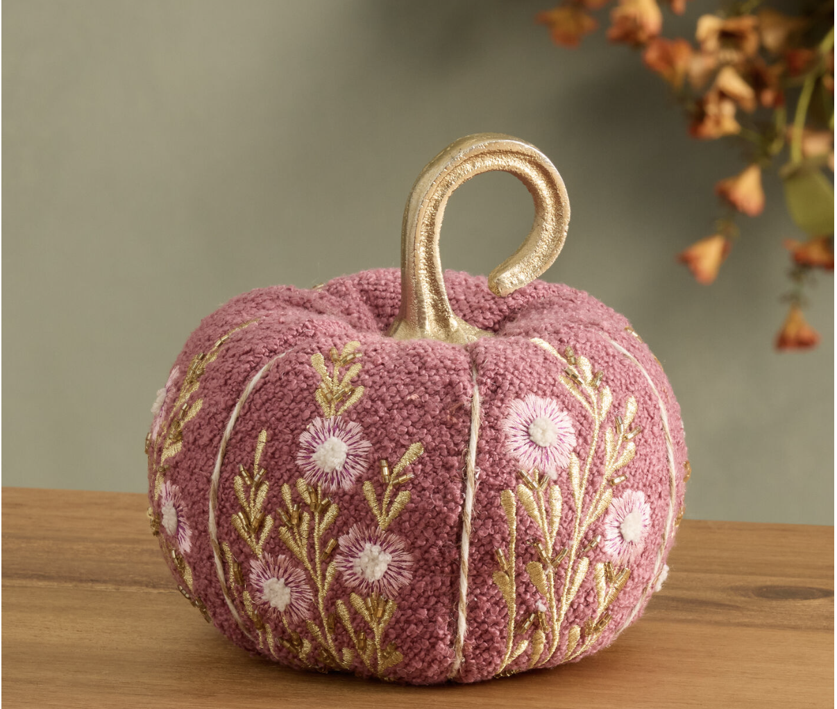 Perfect for shopping with friends, this pink pumpkin features embroidered flowers and a gold stem on a wooden surface.