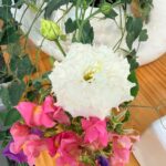 White lisianthus and pink snapdragon flowers in the latest style, on wood with green leaves and white ceramic nearby.