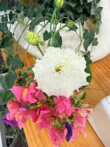 White lisianthus and pink snapdragon flowers in the latest style, on wood with green leaves and white ceramic nearby.