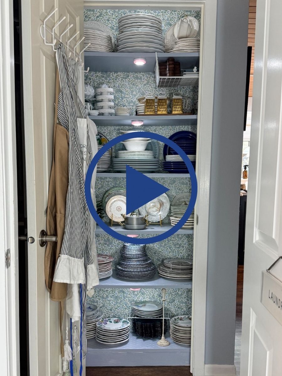 A hall linen closet with shelves neatly stacked with plates, bowls, cups, and linens, viewed through an open door.