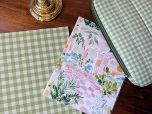 Perfect for shopping organization: green gingham paper, floral folder, and a zipper pouch sit on a desk with a brass lamp.