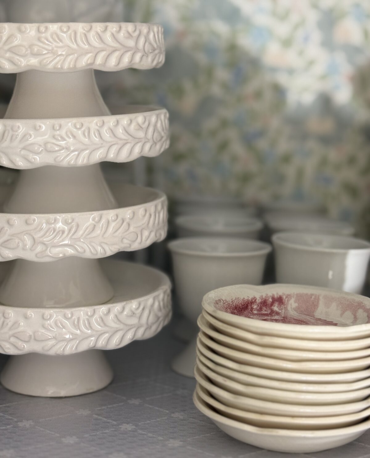 Stacked white cake stands and bowls—perfect for a hosting closet or hall linen closet, against floral wallpaper.