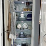 Open pantry with neatly stacked dishes and aprons—it's a true hosting closet ready for any gathering.