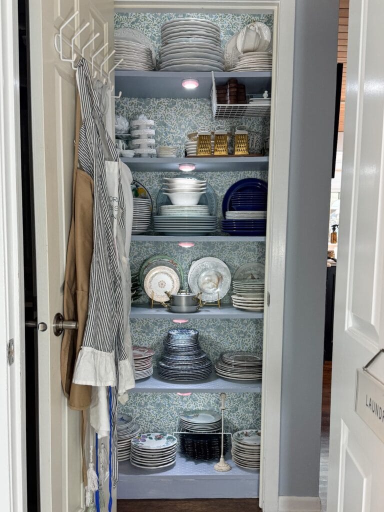 Open pantry with neatly stacked dishes and aprons—it's a true hosting closet ready for any gathering.