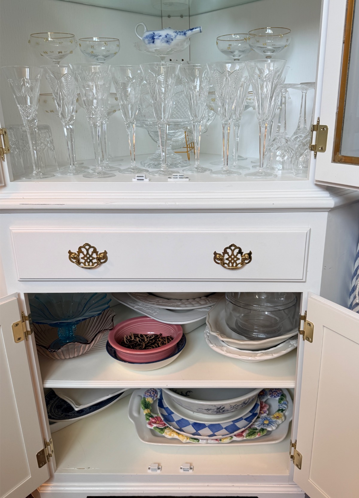 Glassware in a cabinet above china plates, bowls, and serving dishes—perfect for a hosting closet or elegant display.