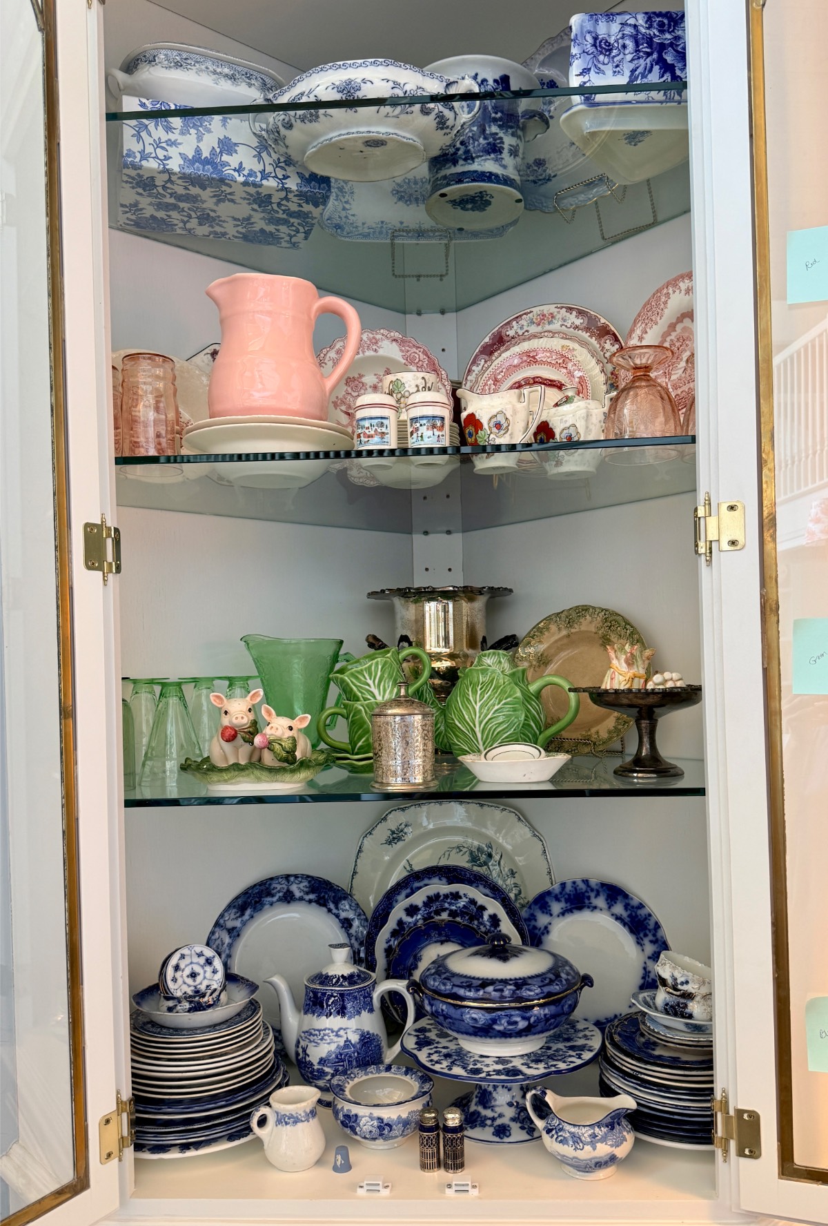 A glass cabinet, like a hosting closet, displays assorted vintage china, teacups, bowls, and colorful glassware.