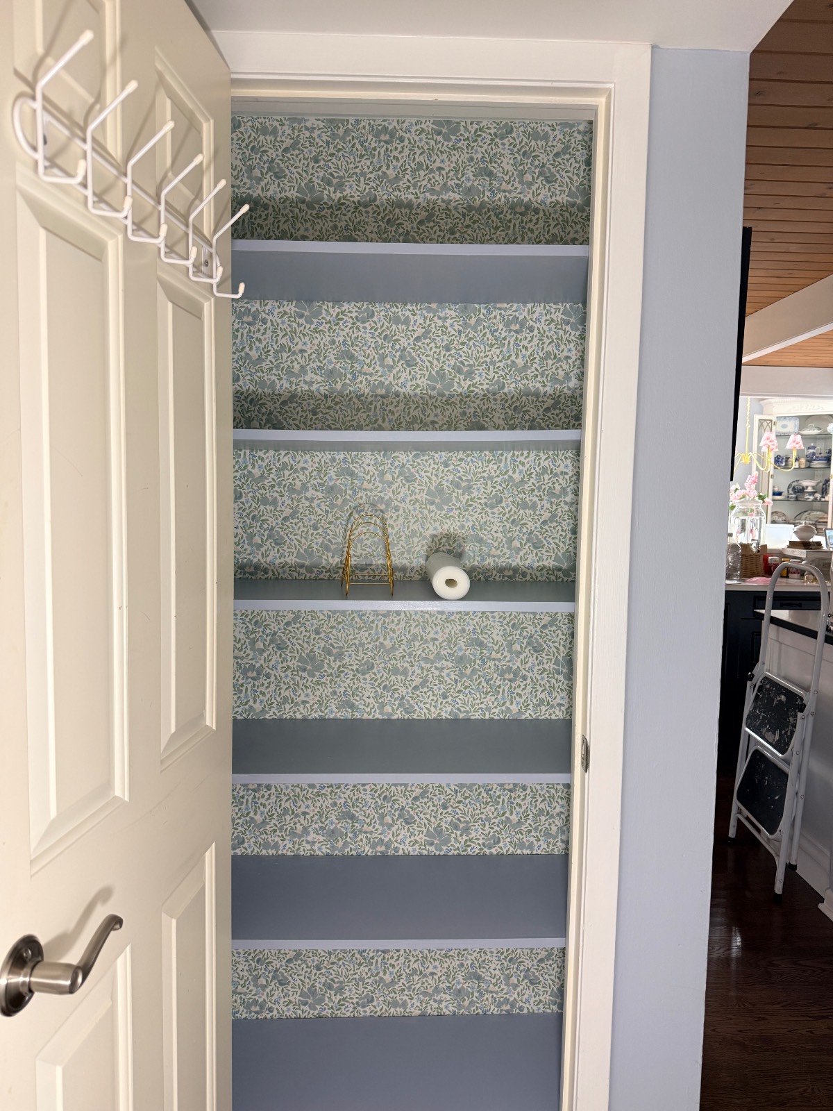 A hall linen closet with blue floral shelves, wire basket, and toilet paper—perfect as a tidy hosting closet.
