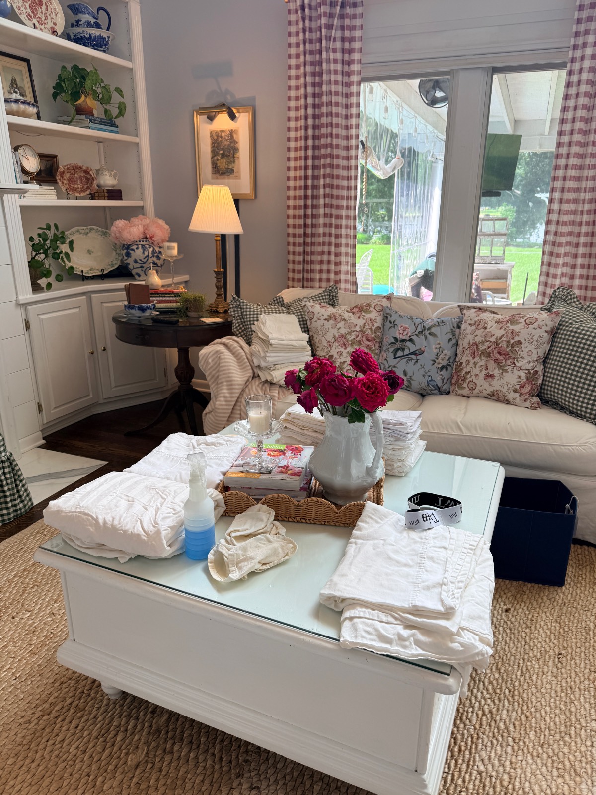 A cozy living room with folded laundry from the hall linen closet, flowers, and cleaning supplies on a white coffee table.