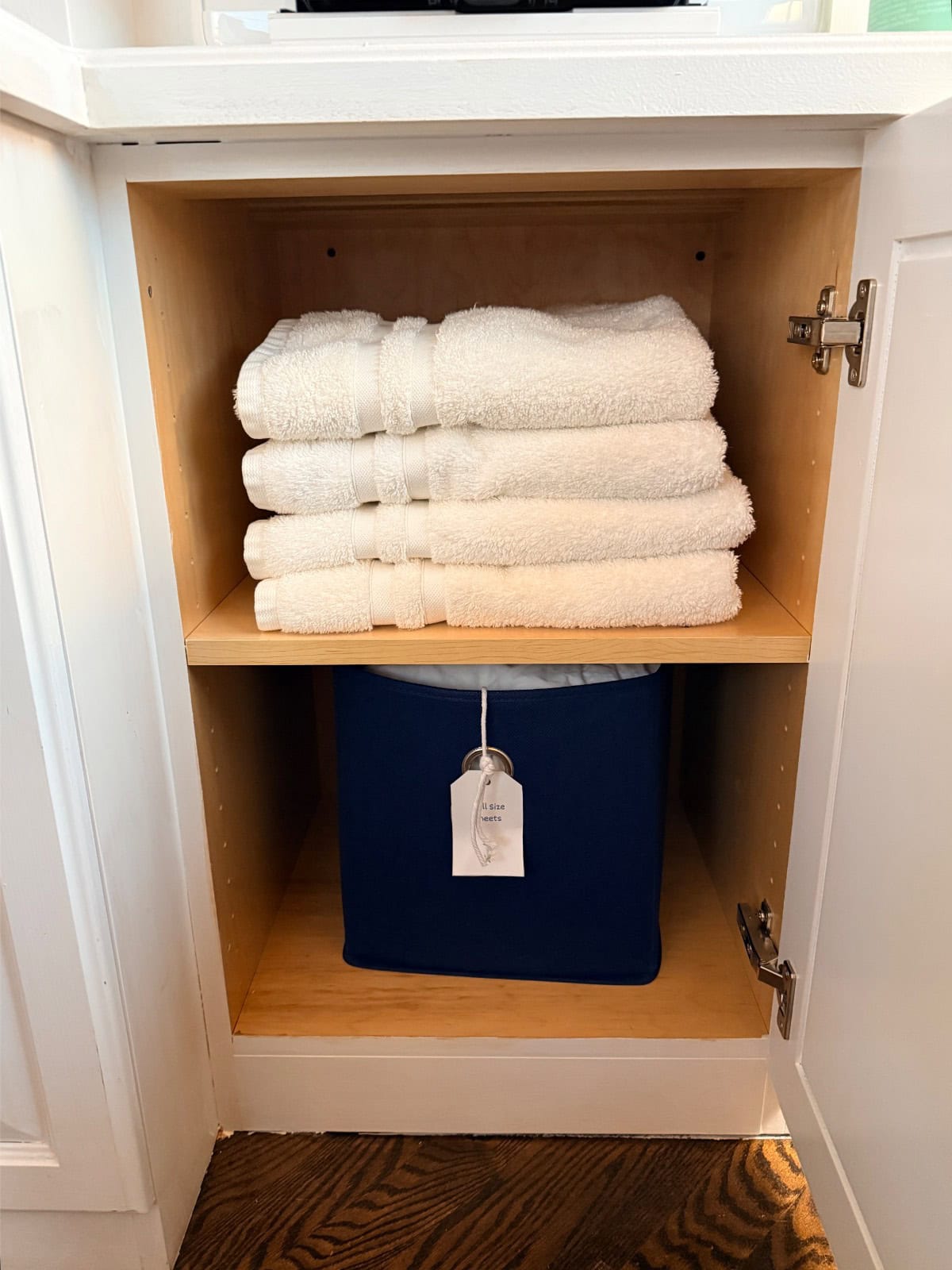 Four folded white towels on a shelf above a blue bin, perfect for a hall linen closet's organized transformation.