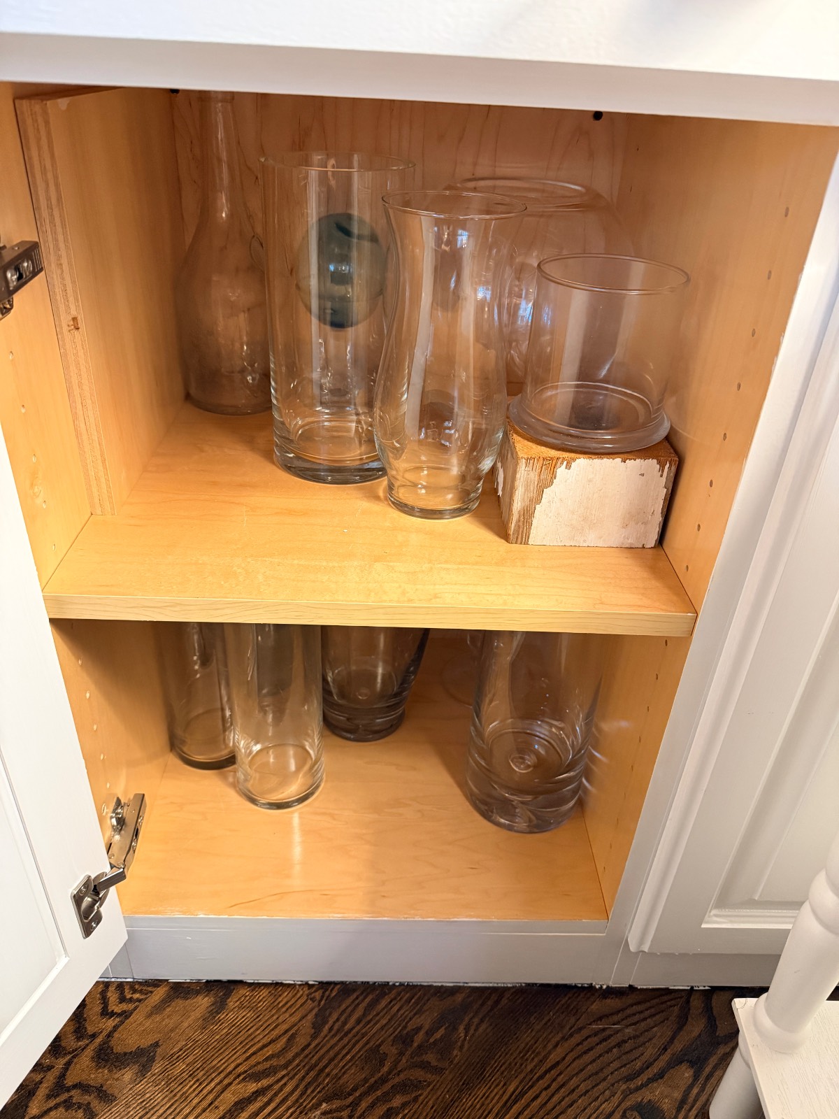 Two shelves in a hall closet cabinet store empty glass vases of various shapes and sizes.