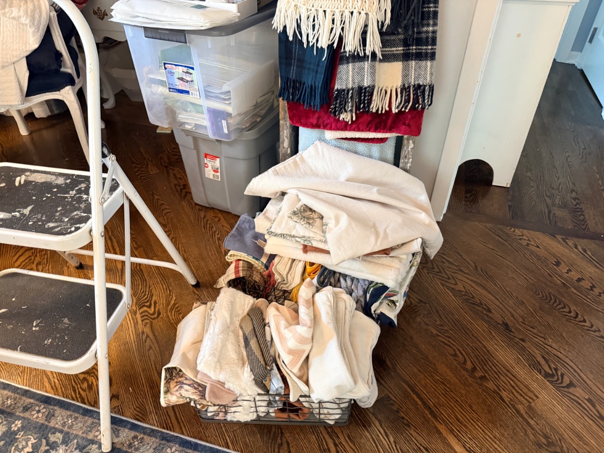 A metal basket of folded linens sits on a wood floor, ready for your next linen closet transformation.
