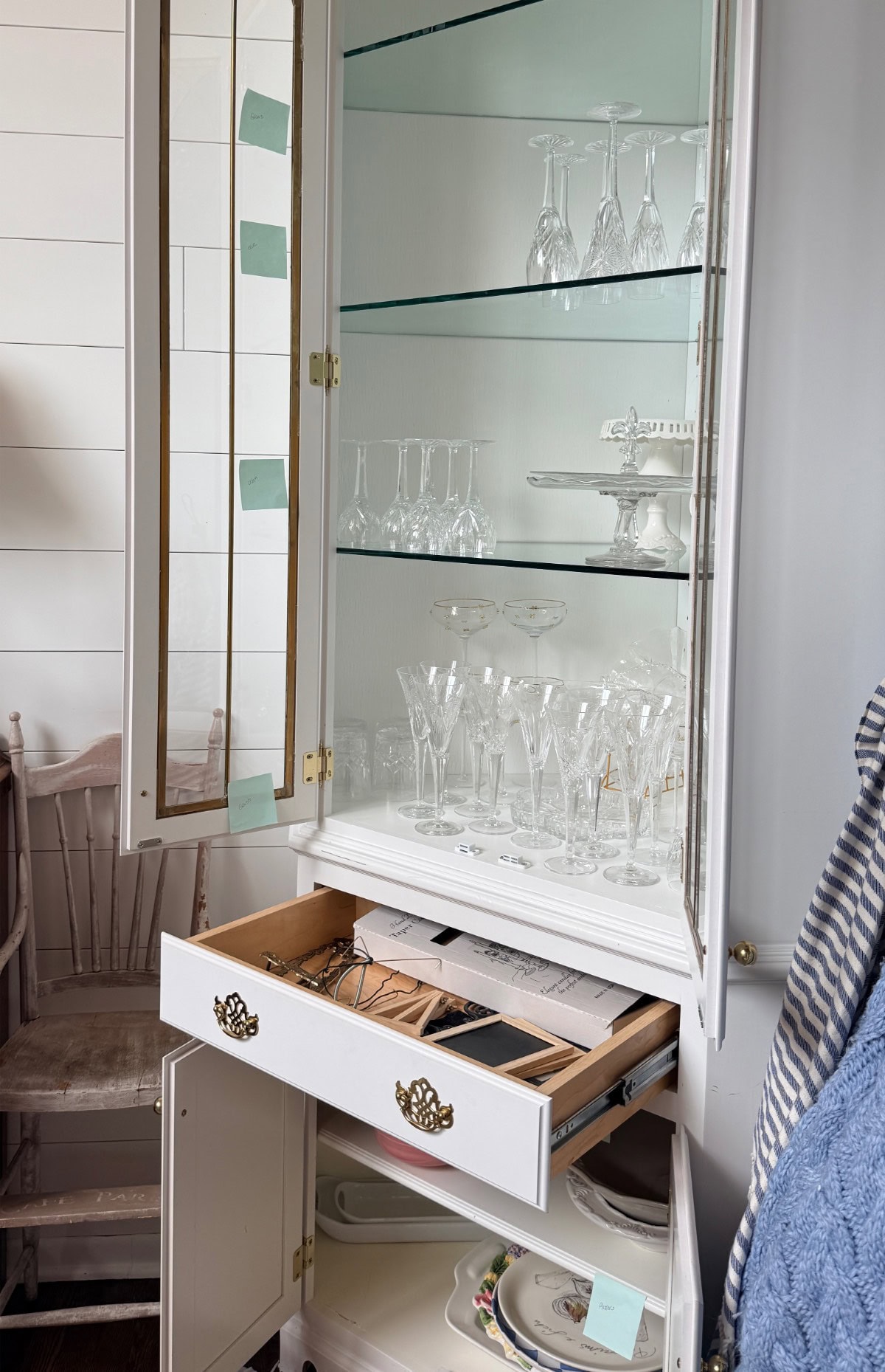 Open china cabinet doubles as a hosting closet, displaying glassware above and storing plates and utensils below.