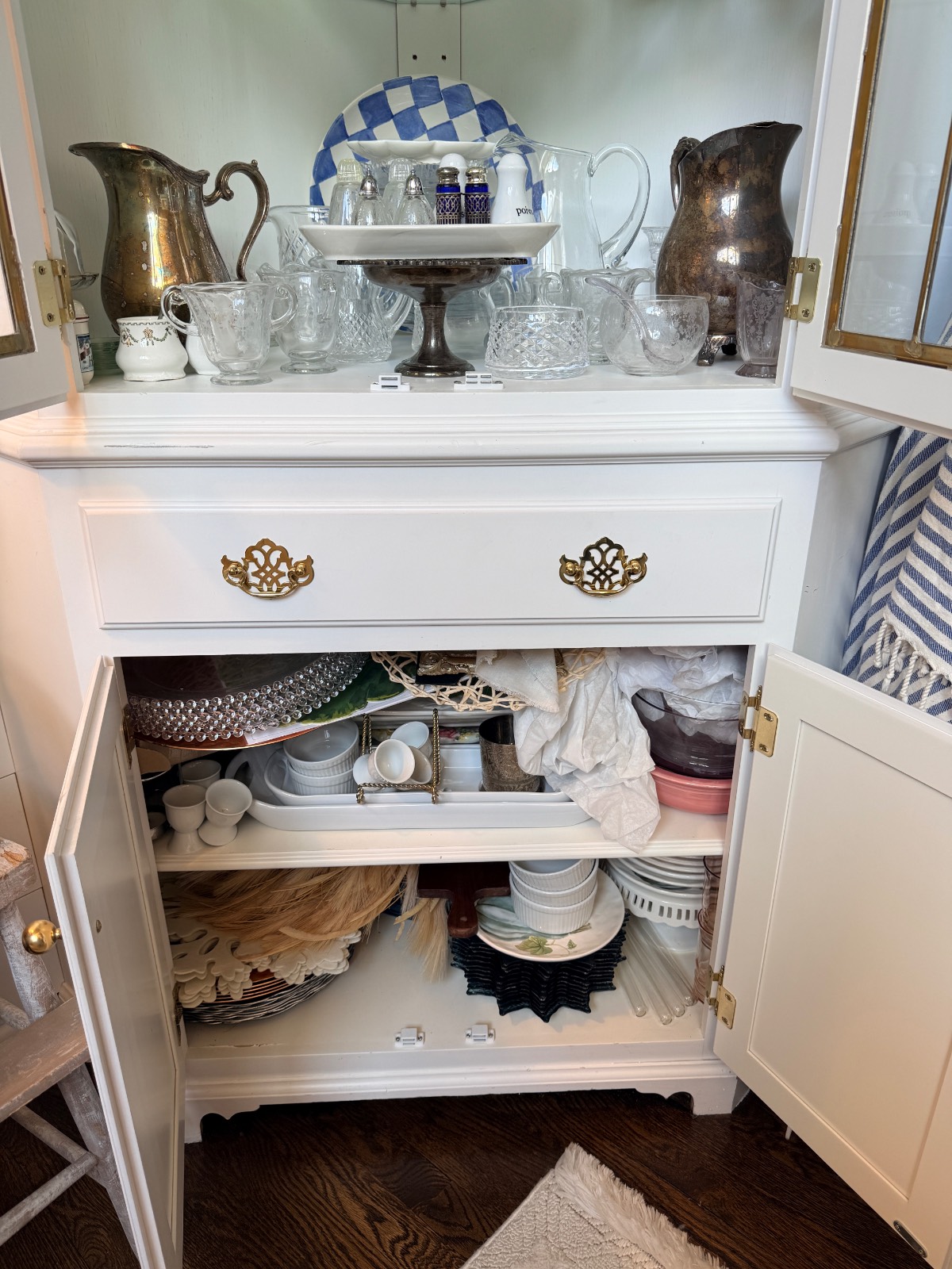 A white cabinet transformed into a hosting closet; glassware above, baskets and plates neatly arranged below.