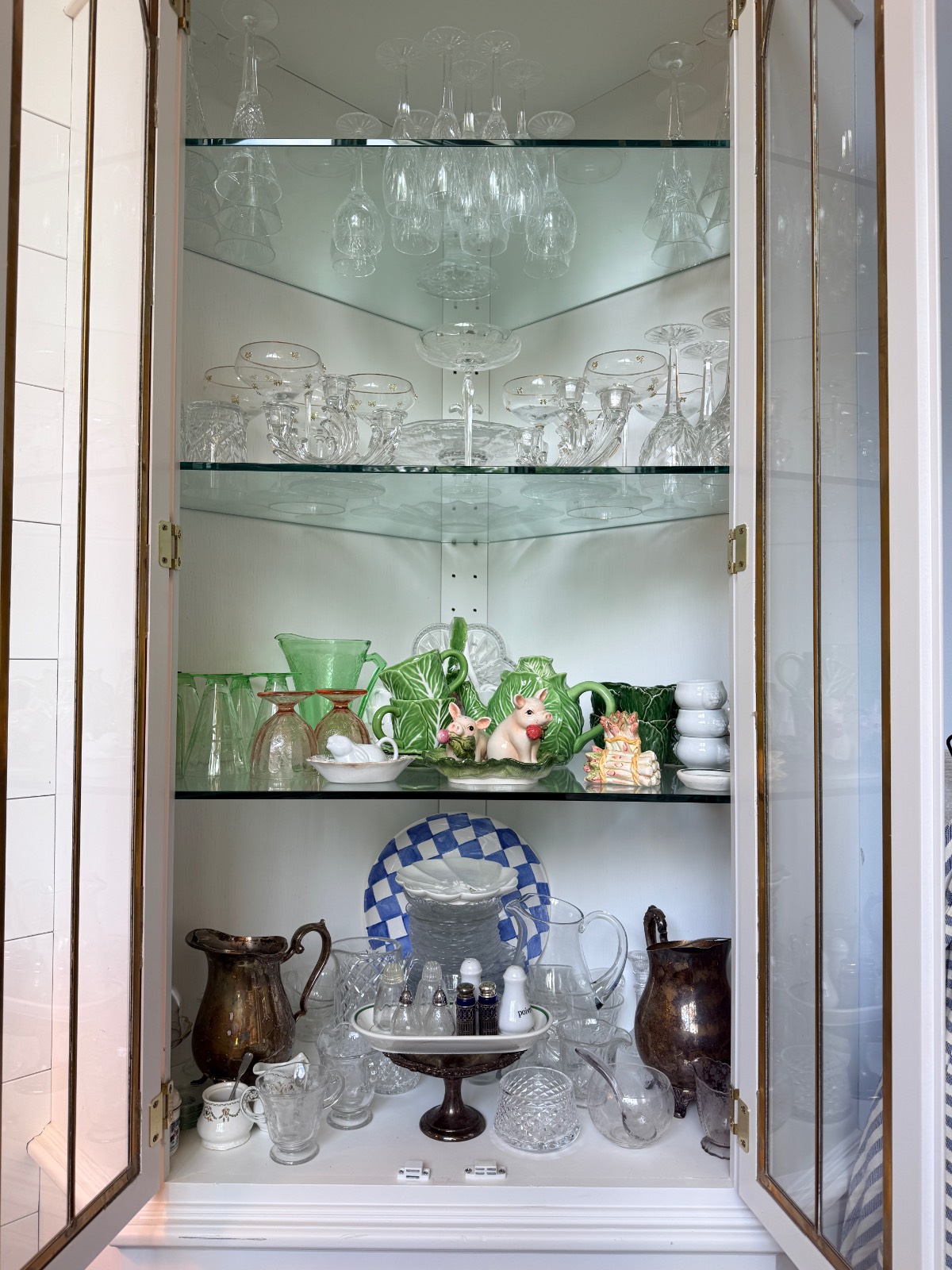 Glass cabinet serves as a stylish hosting closet, displaying glassware, porcelain, green cups, and metal pitchers.