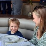 A smiling child sits at a restaurant table with a woman, both enjoying the latest dishes and looking happy and relaxed.