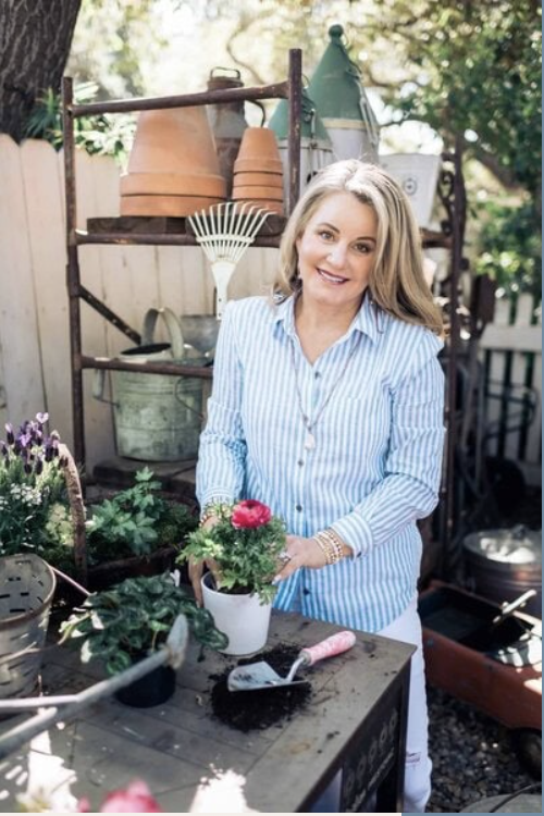 Woman in striped shirt tries the latest gardening tools, standing by a table with plants and soil, smiling at the camera.