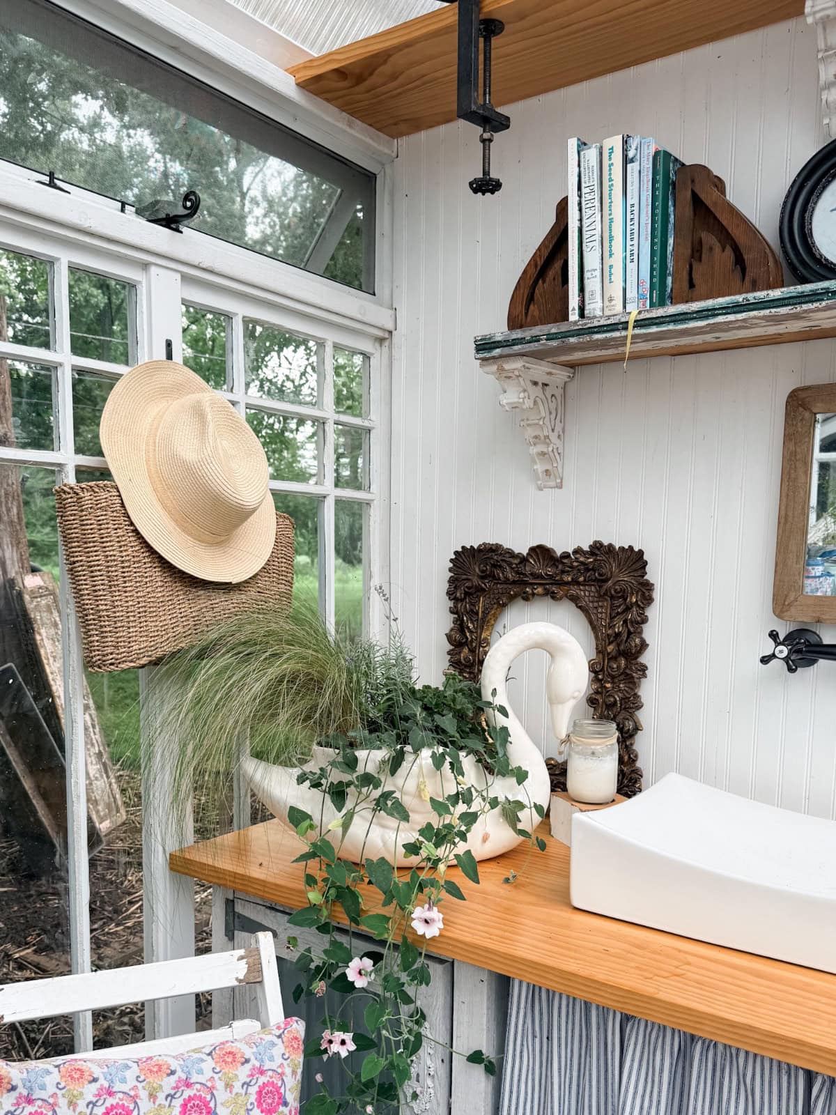 A cozy sunroom corner with vintage finds, lush plants, books, a hat, and a striped changing pad for summer styling.