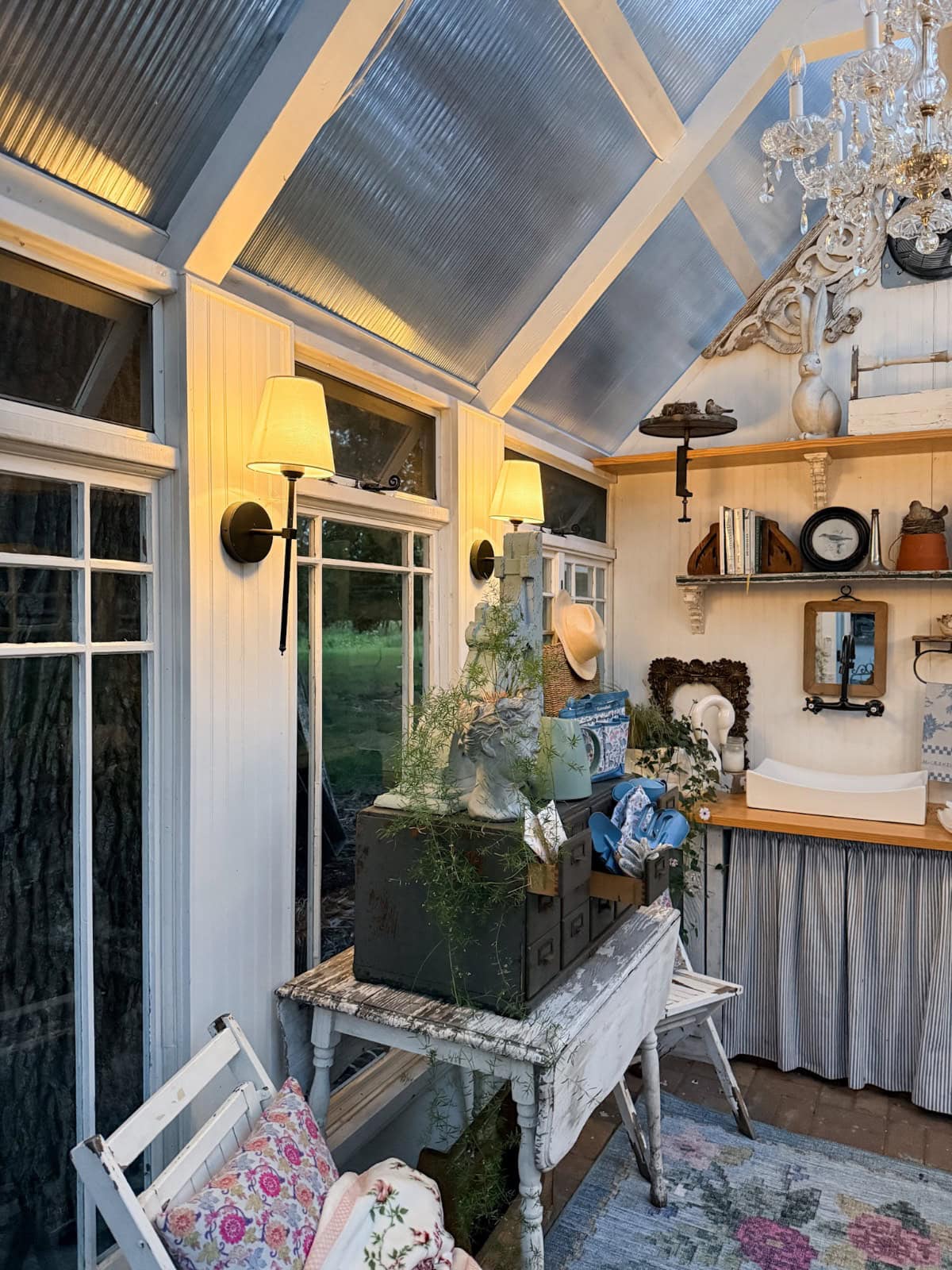 Cozy garden shed with vintage finds, rustic desk, plants, wall lamps, shelves, and chandelier for summer styling.