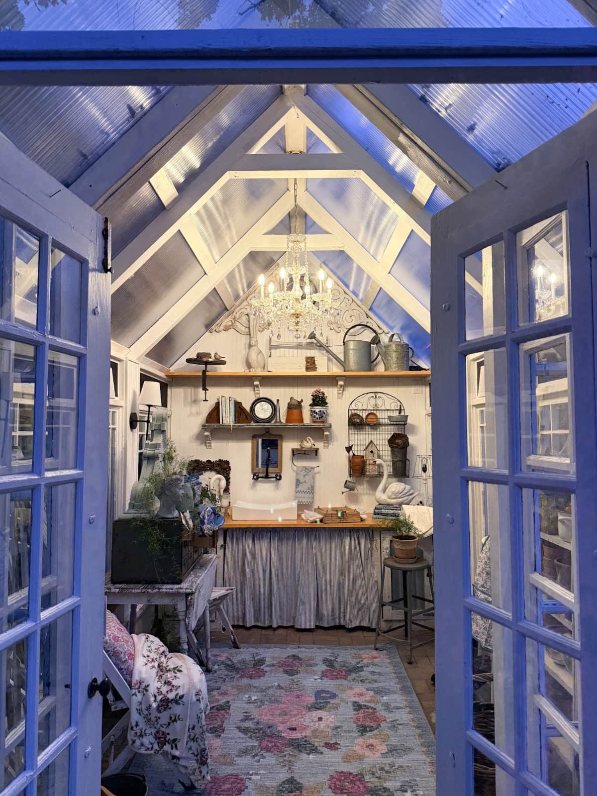 Cozy greenhouse interior with a chandelier, floral rug, and French doors styled with charming vintage finds.