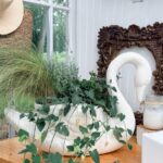 White swan planter with green plants on a table, vintage finds nearby, by a framed mirror and mason jar candle.
