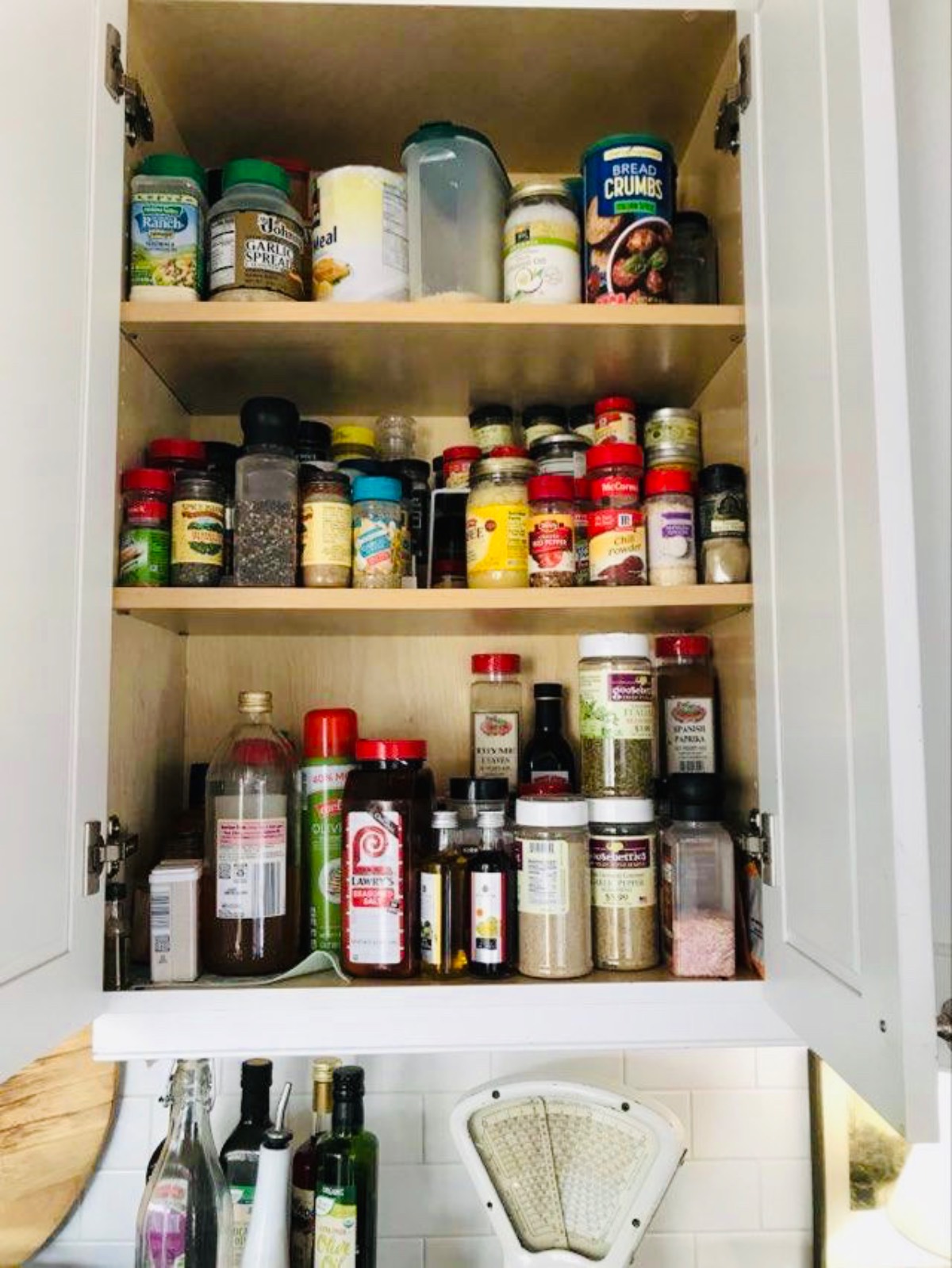 An open kitchen cabinet holds assorted spices and sauces—spot some things to throw away right now on its three shelves.