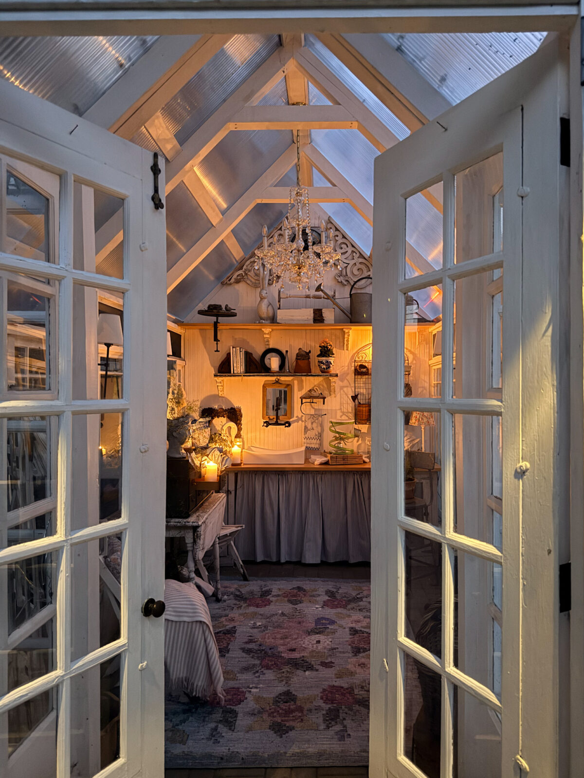 French doors open to a cozy, warmly lit room with vintage finds, a chandelier, and shelves of curiosities.