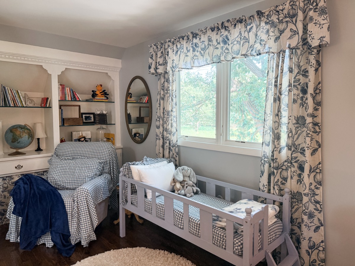 Cozy third bedroom: a child’s room with bed, stuffed animals, bookshelves, armchair, and floral curtain window.