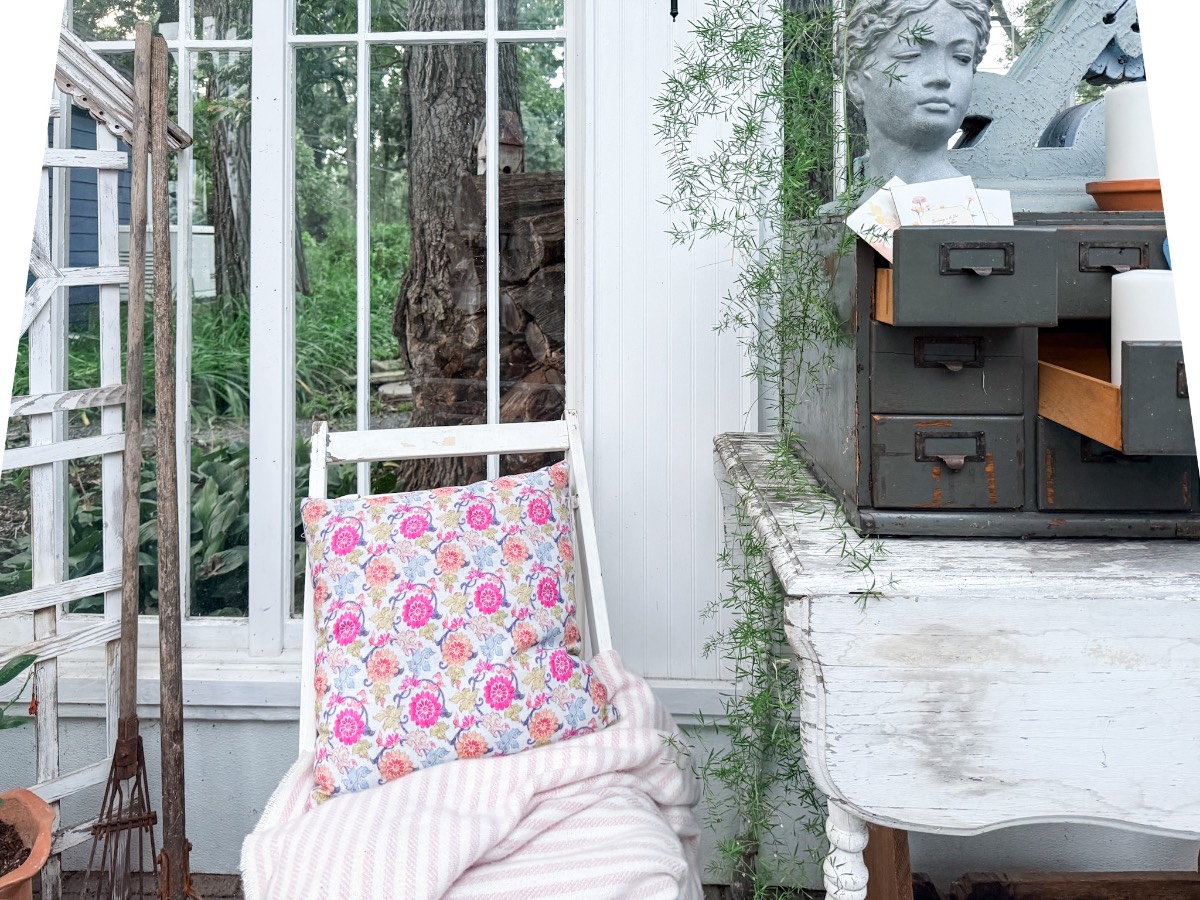 A floral pillow on a white chair beside vintage finds and a gray bust, perfect for summer styling in a sunlit room.
