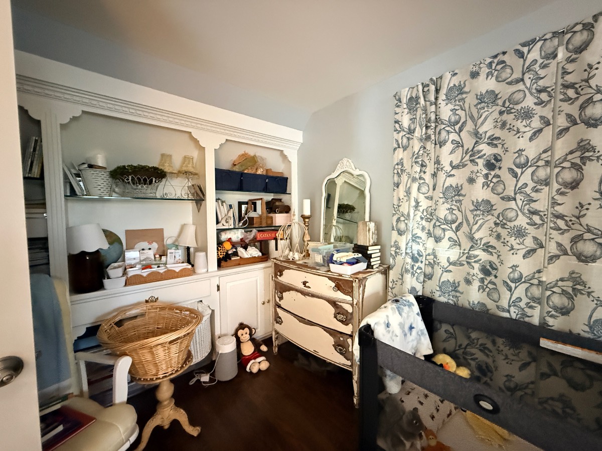 Cozy nursery room with vintage furniture, baby crib, toys, and blue floral curtains in a charming third bedroom.