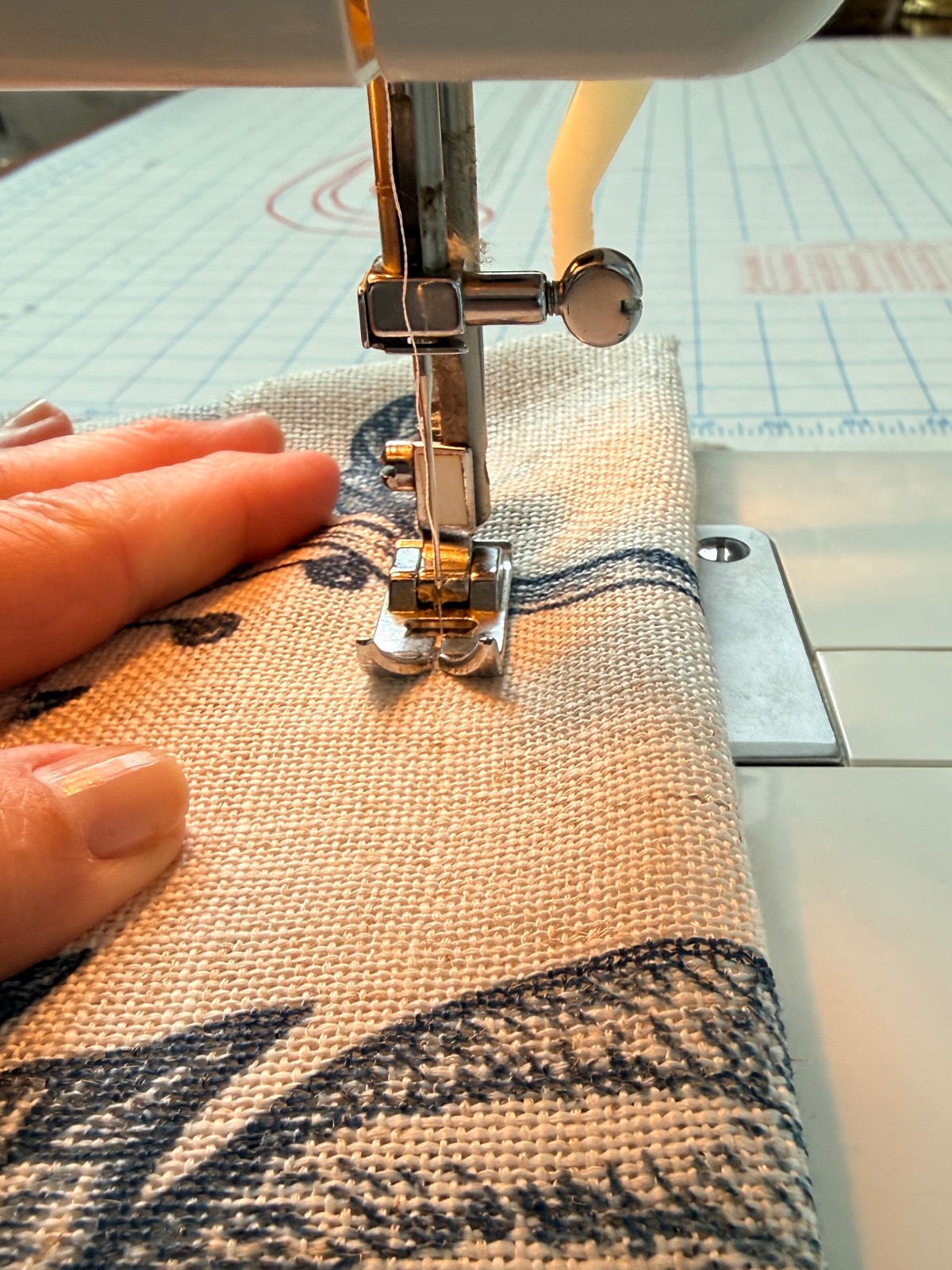 Close-up of a hand guiding fabric on a sewing machine, creating cozy touches for a third bedroom or family suite.