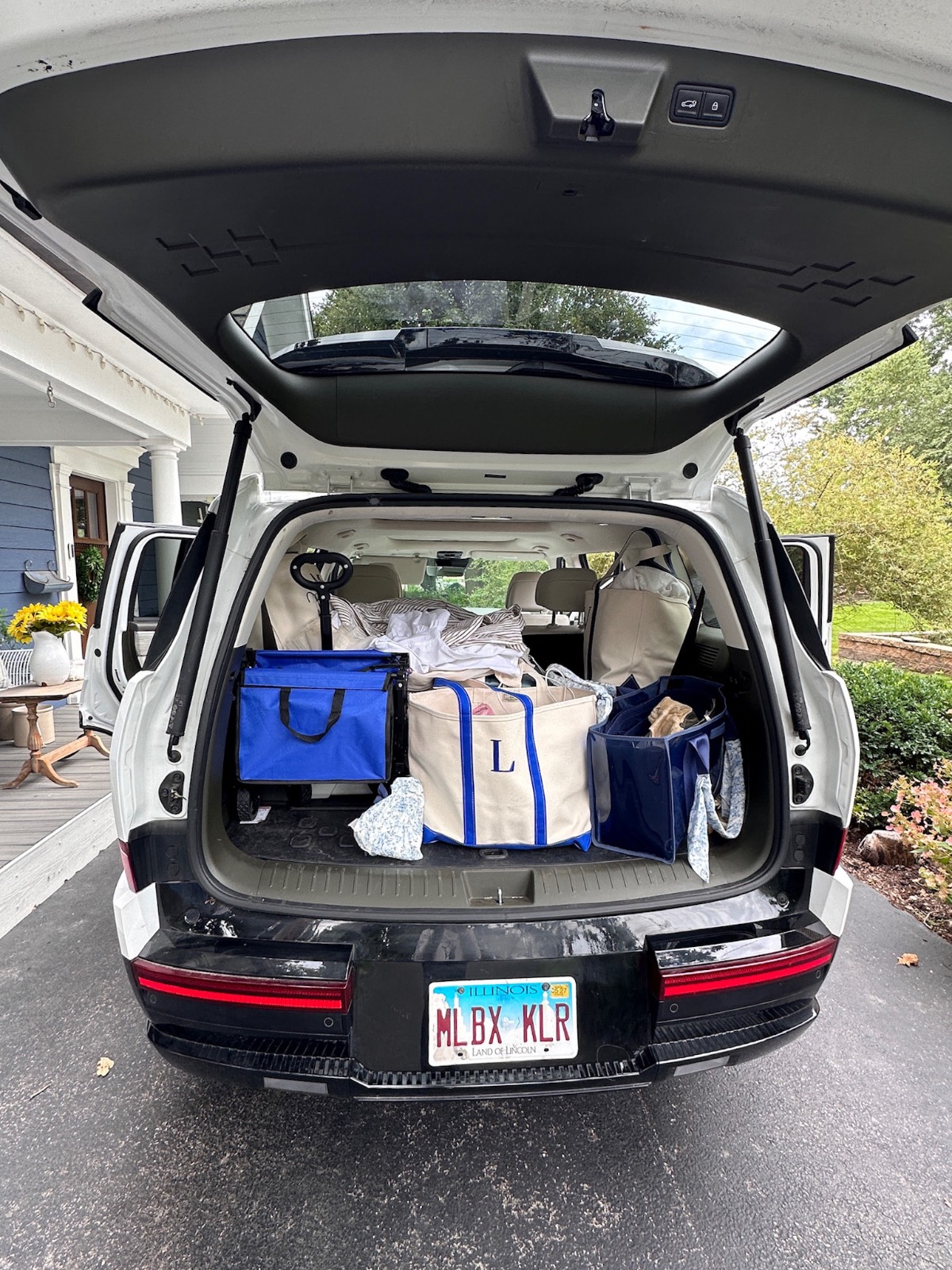 SUV trunk open, packed with bags, parked in a driveway near a blue house found at the cottage mercantile market.