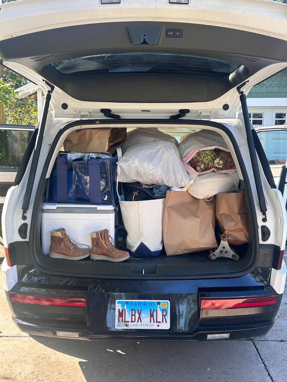 Open SUV trunk packed with bags, boxes, boots, and a plant from the Found Cottage Mercantile Market. Illinois plate visible.