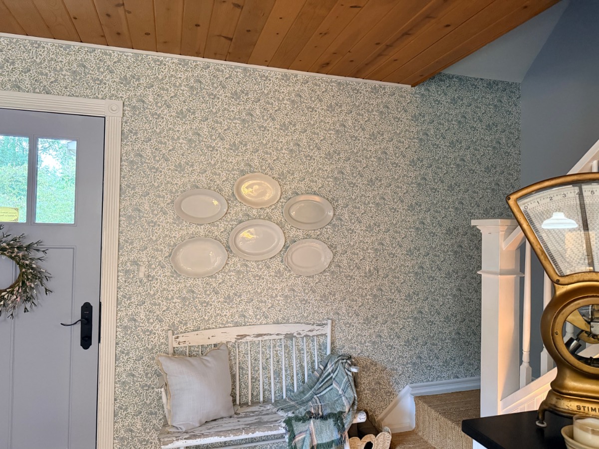 Ironstone plate wall above a vintage bench in a wallpapered entryway
