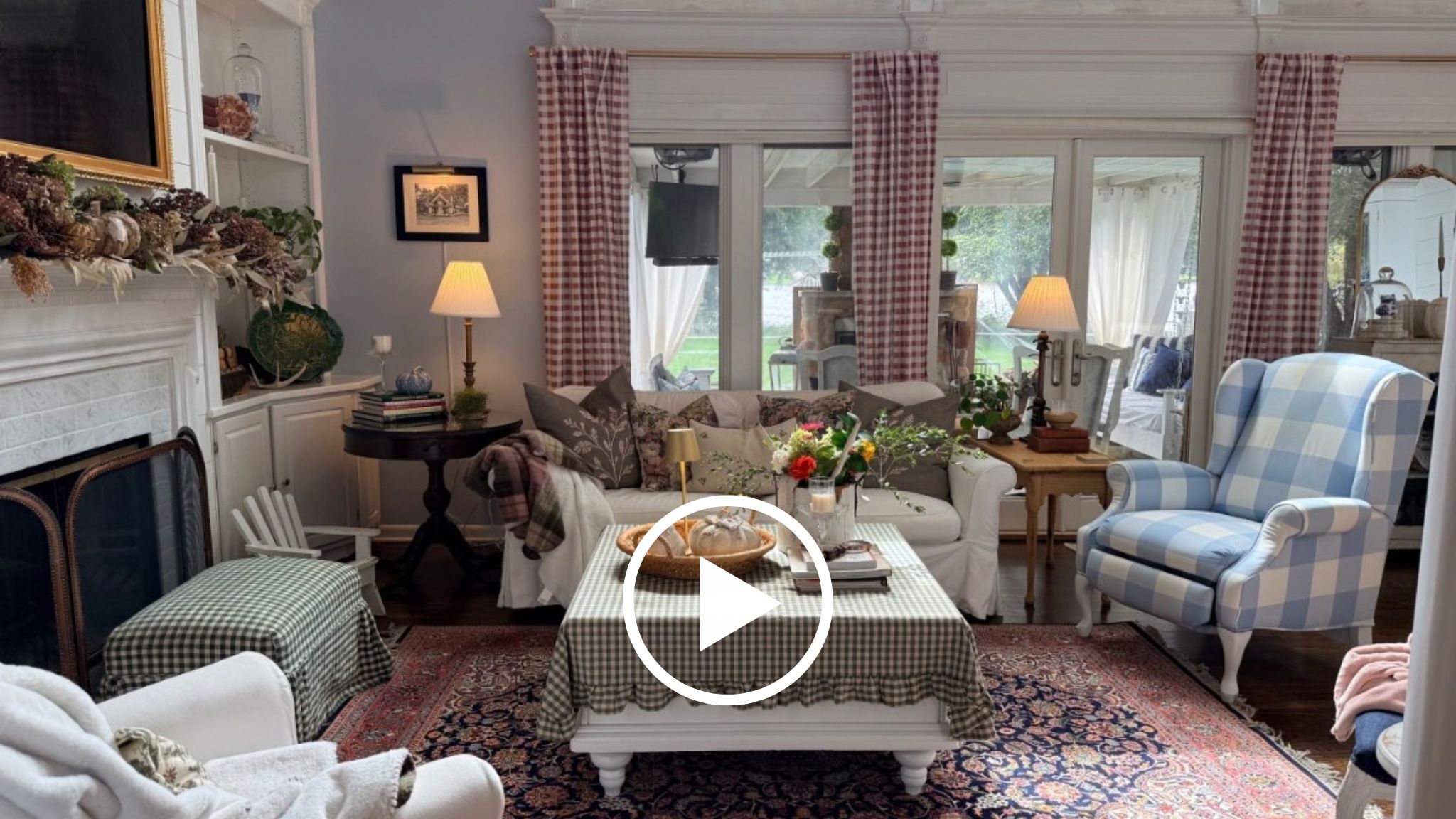 Cozy living room with patterned chairs, cranberry decor, coffee table, flowers, lamps, and plaid-curtained windows.