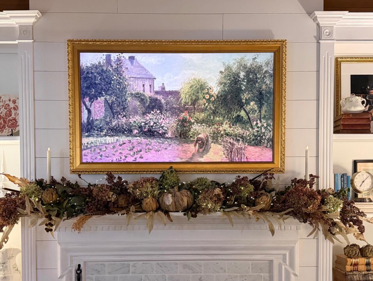 Framed painting of a colorful garden above a white fireplace with muted fall decor, dried flowers, and foliage.