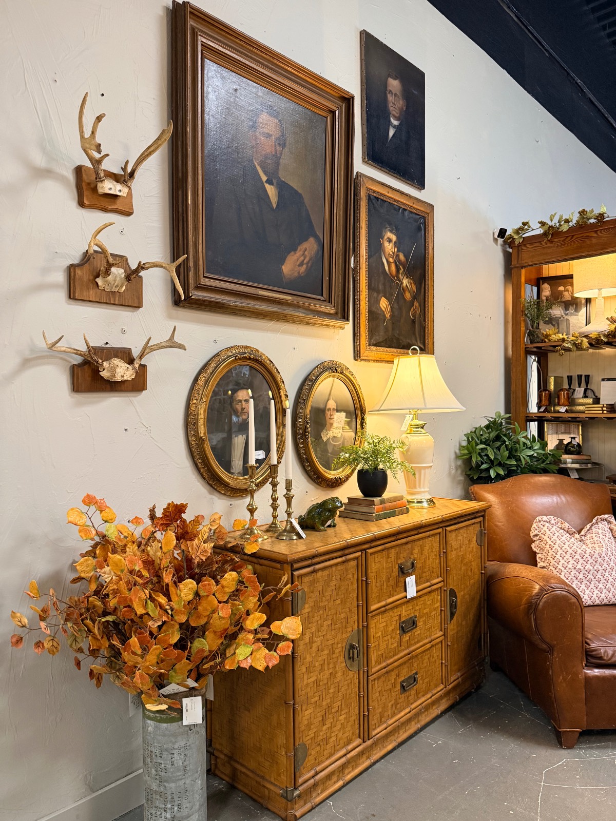 Vintage-style room with found treasures, cottage portraits, antlers, sideboard, plants, lamp, and leather chair.