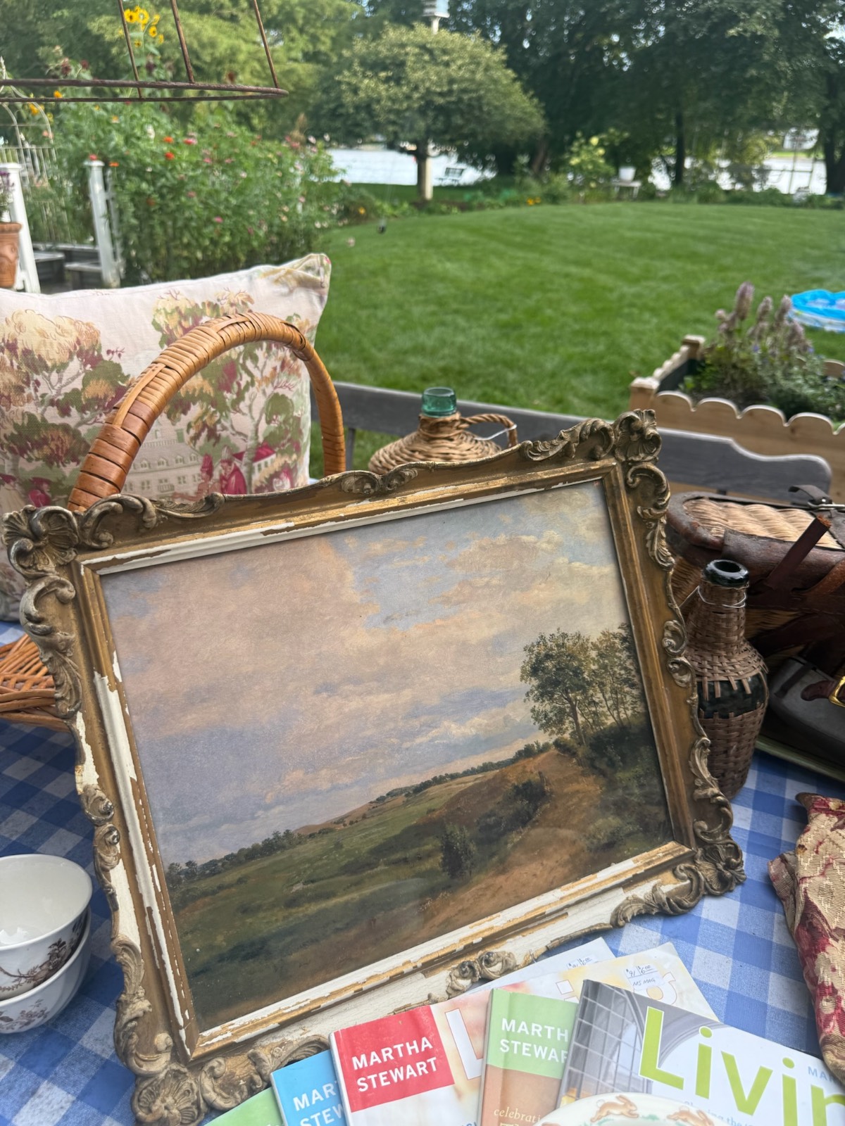 Vintage market finds including framed landscape painting on table with books, basket, pillows—evoking a found cottage mercantile market charm.