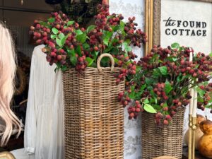 Two wicker baskets display the latest faux berry branches outside a shop with a “the Found Cottage” sign.