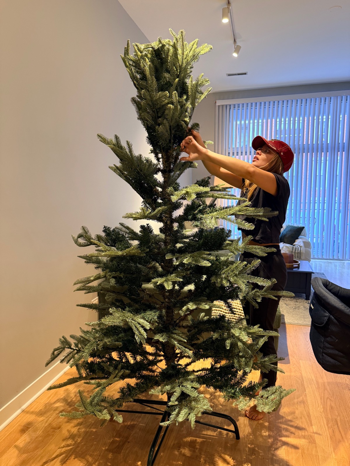 A person in a red cap adjusts the top of an artificial Christmas tree decorated with firecracker lights.