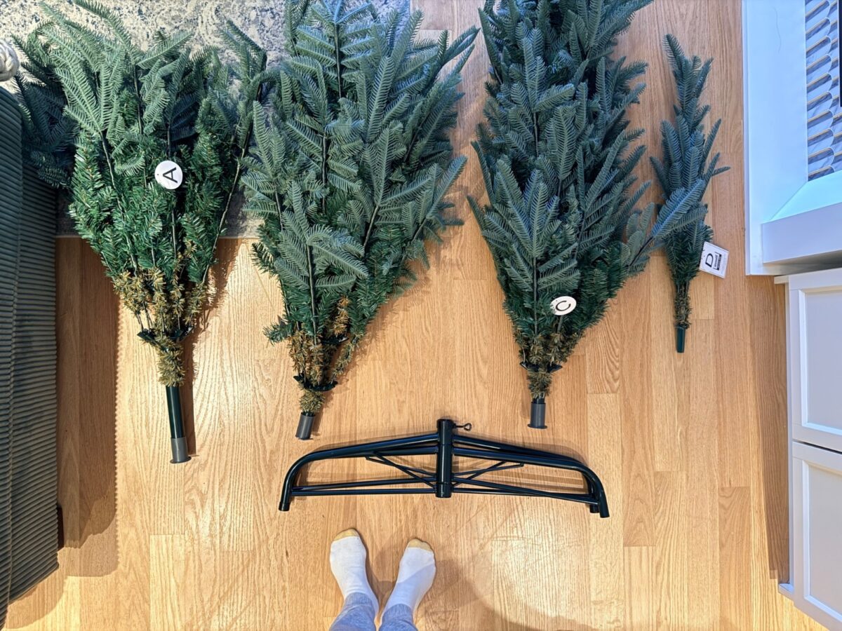 Four sections of a firecracker lights Christmas tree labeled A through D, with a metal stand, laid out on a floor.