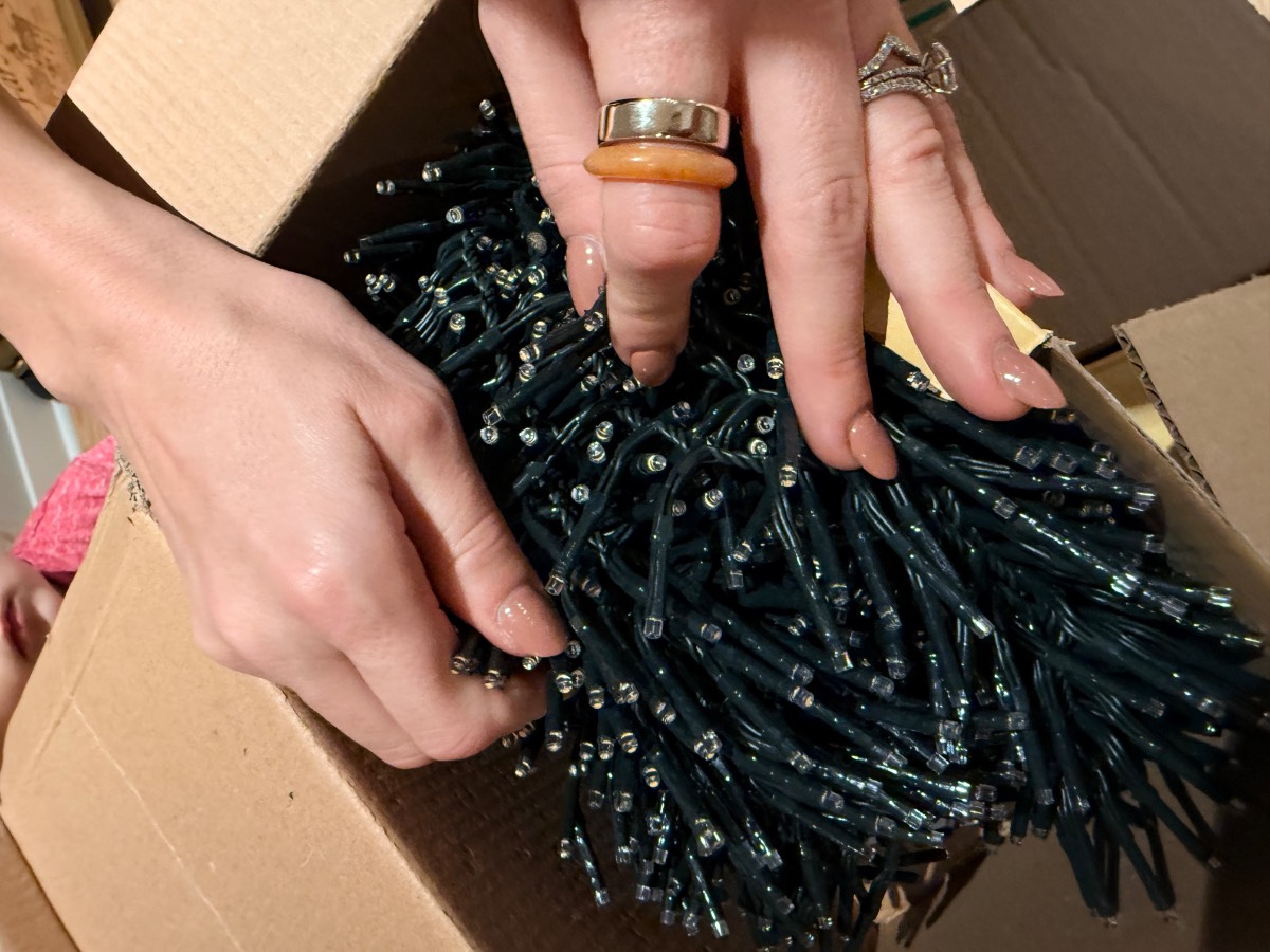 Hands holding a bundle of green-wired firecracker lights inside a cardboard box.