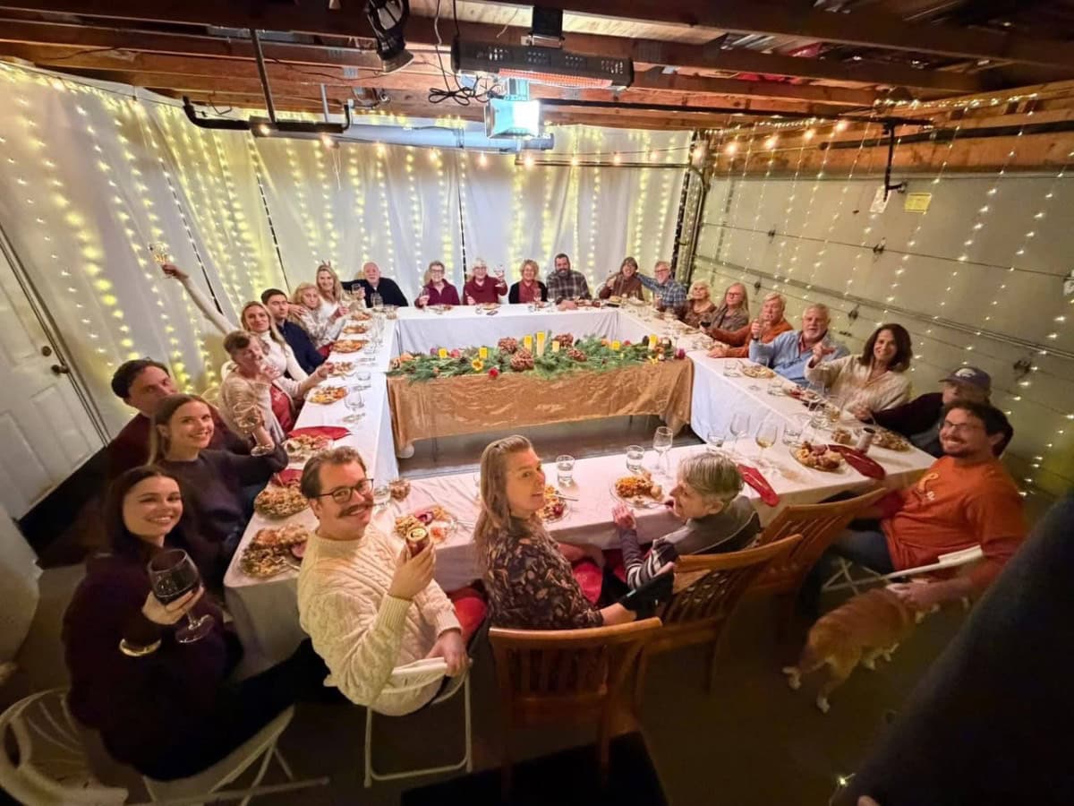 A large group seated at U-shaped tables with greenery and lights, perfect for small house thanksgiving dining.
